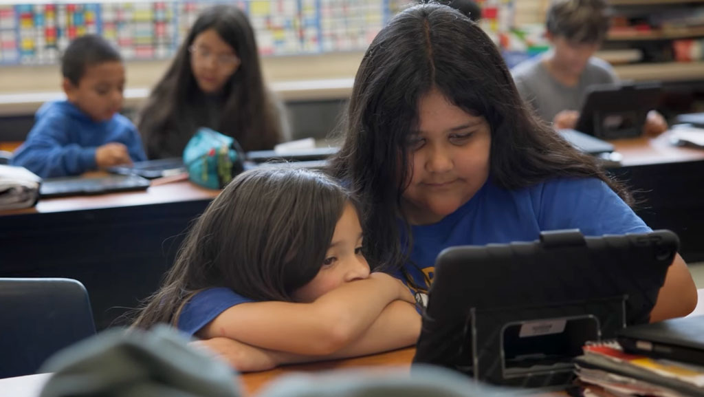 Older student helping a younger student on an iPad