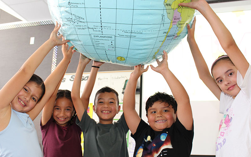 group of elementary students interacting with a large globe