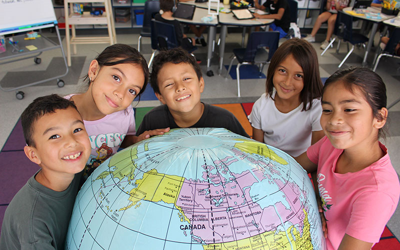 group of elementary students interacting with a large globe