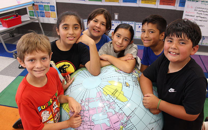 group of elementary students interacting with a large globe