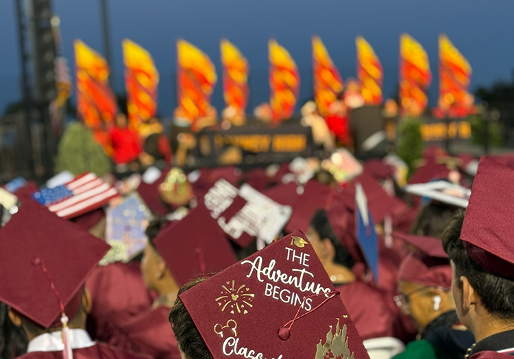 graduation day. an ocean of burgundy graduation caps with the focus on one that says, the adventure begins