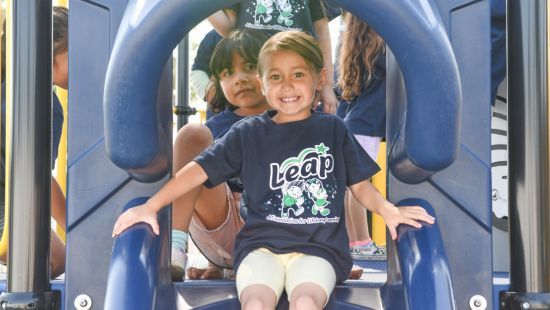 Little 3 year old girl wearing LEAP shirt in a slide.